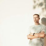 a man standing in front of a white wall with his arms crossed