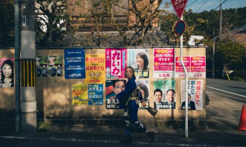 a man walking down a street past a wall covered in posters