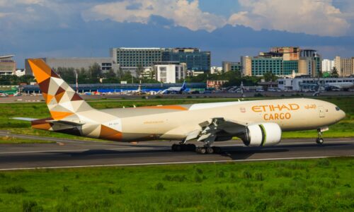 Etihad cargo airplane taxiing on runway with cityscape background