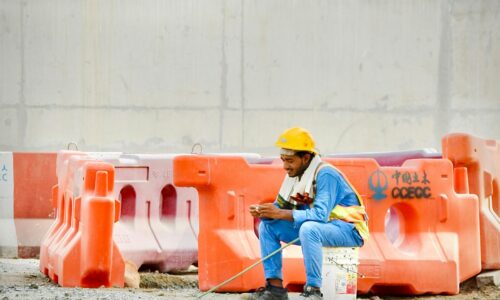 Construction worker in hard hat sits on bucket using phone.