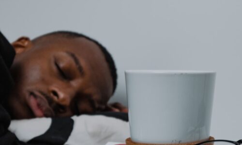 a man sleeping on top of a stack of books next to a cup of coffee