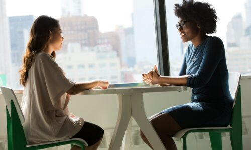 two women sitting beside table and talking
