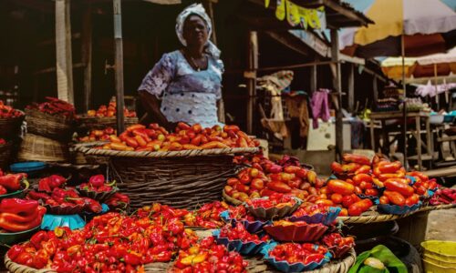 man in white long sleeve shirt and white hat standing in front of fruit stand