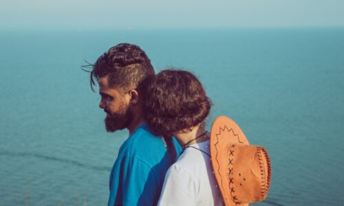 man in blue t-shirt standing in front of woman beside body of water