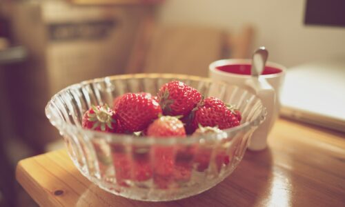 bowl of strawberries beside white mug on table