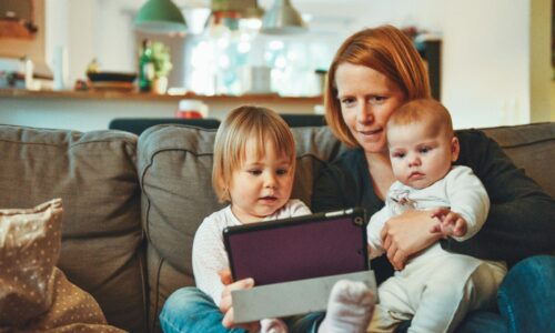 two babies and woman sitting on sofa while holding baby and watching on tablet